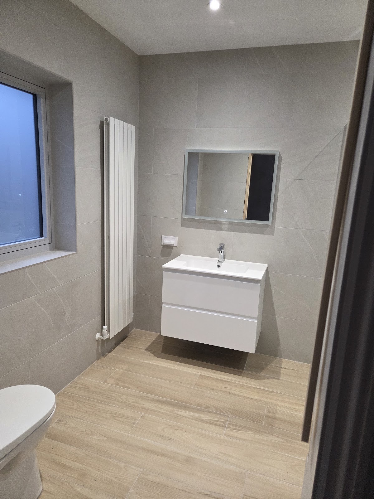 Finished bathroom with large-format grey wall tile and wood-look floor