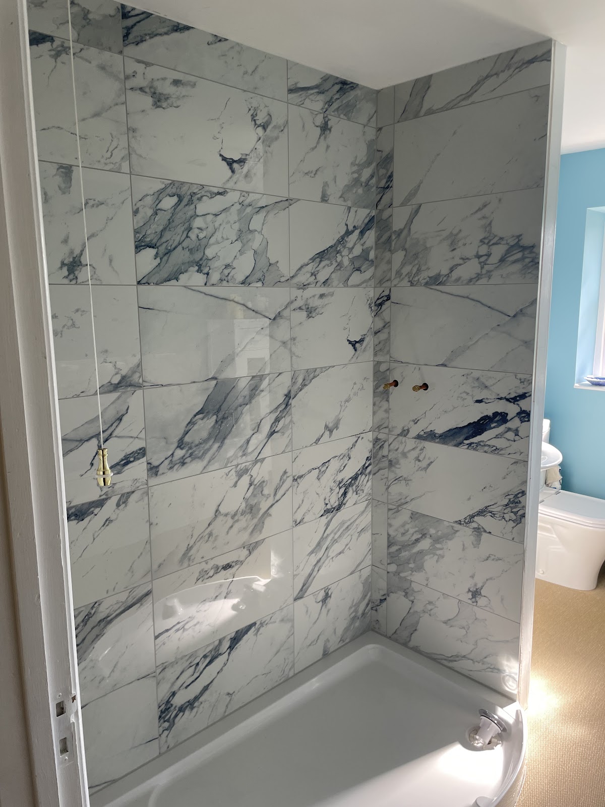 Premium marble-effect large-format shower and bath surround with brushed brass fittings